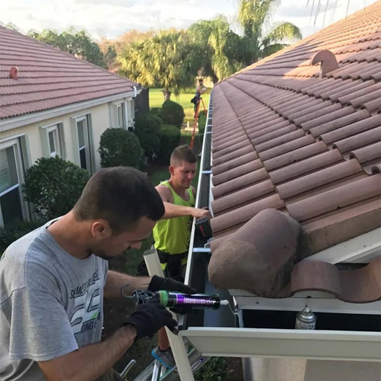 Two men working on a roof gutter.